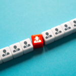 A row of white cubes with icons of people in suits, symbolizing uniform individuals, with a single red cube depicting a figure in a hat and trench coat, representing an undercover or hidden character among the crowd. This visually highlights the concept of an infiltrator or hidden element within a larger group, akin to the role of cancer-associated fibroblasts (CAFs) supporting tumor growth in the tumor microenvironment.