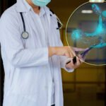 A doctor wearing a white coat and a surgical mask is holding a tablet and pointing at it. In the foreground, a digital hologram of a stomach, composed of a glowing blue wireframe, is superimposed. The image suggests the use of advanced medicine in gastroenterology or digestive health.