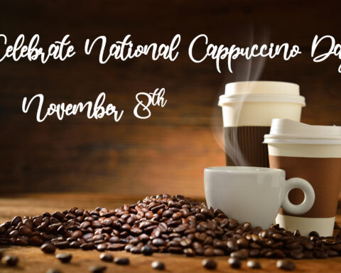 Celebrate National Cappuccino Day on November 8th. A cozy arrangement of a steaming white coffee cup and two to-go coffee cups surrounded by coffee beans, set against a warm, rustic wooden background.