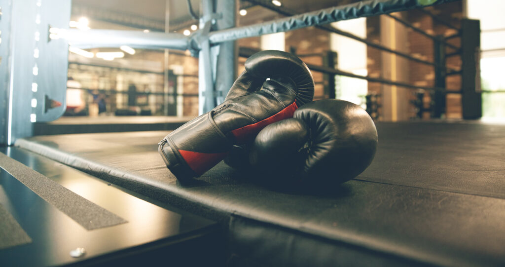 Black boxing gloves resting on a boxing ring mat in a gym, symbolizing the fight against age-related muscle loss as highlighted in the article 'How to Understand and Combat Age-Related Muscle Loss.