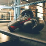 Black boxing gloves resting on a boxing ring mat in a gym, symbolizing the fight against age-related muscle loss as highlighted in the article 'How to Understand and Combat Age-Related Muscle Loss.