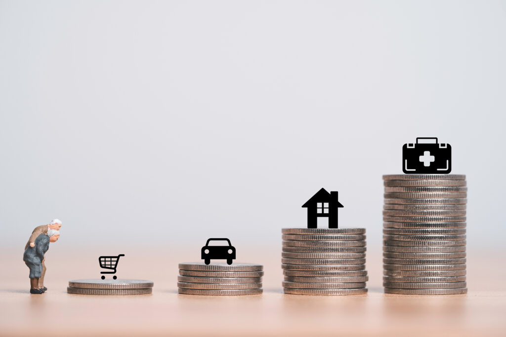 A conceptual image showing stacks of coins of varying heights representing the increasing financial burdens of aging. On the smallest stack stands a miniature elderly figure, symbolizing limited resources. Icons of a shopping cart, car, house, and medical briefcase are placed on progressively taller stacks, illustrating the growing costs of essentials, housing, transportation, and healthcare associated with aging. The background is minimalist and neutral, emphasizing the financial theme.