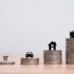 A conceptual image showing stacks of coins of varying heights representing the increasing financial burdens of aging. On the smallest stack stands a miniature elderly figure, symbolizing limited resources. Icons of a shopping cart, car, house, and medical briefcase are placed on progressively taller stacks, illustrating the growing costs of essentials, housing, transportation, and healthcare associated with aging. The background is minimalist and neutral, emphasizing the financial theme.