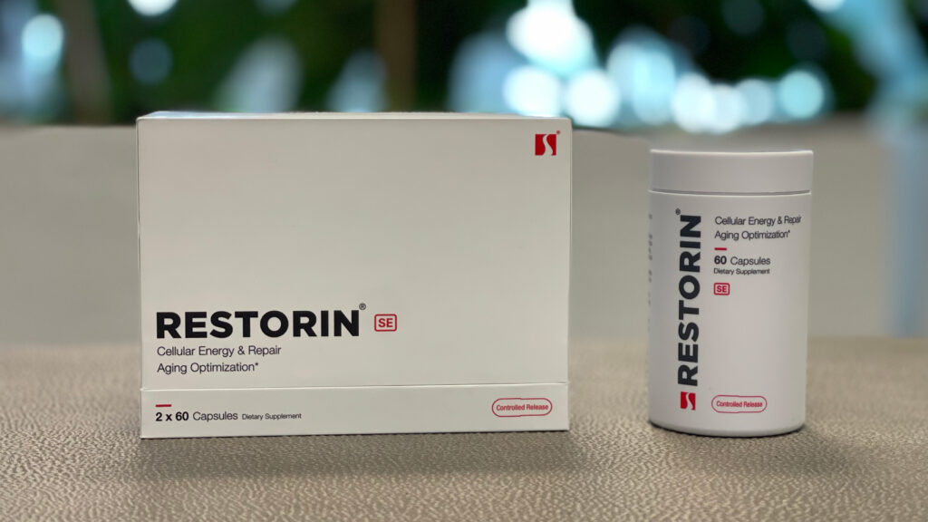 A promotional image showcasing the RESTORIN® product packaging and bottle. The white box with bold black text "RESTORIN SE" and the accompanying bottle labeled "Cellular Energy & Repair Aging Optimization" are placed on a neutral surface, with a blurred natural background that emphasizes innovation and health. The sleek, minimalist design of the packaging highlights RESTORIN®'s focus on advanced scientific research targeting the root causes of aging, including mTOR modulation, senolytics, and sirtuin activation.