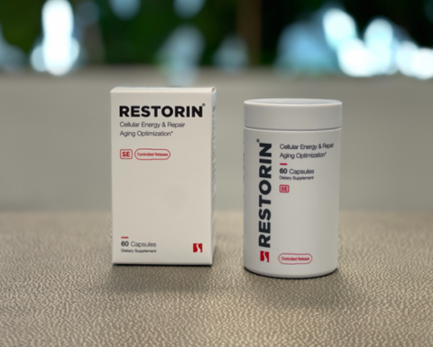 RESTORIN product display showcasing its premium design and packaging. The image features a white rectangular box labeled 'RESTORIN - Cellular Energy & Repair, Aging Optimization,' alongside a cylindrical bottle with matching minimalist aesthetics. Both are positioned on a sleek surface, with a blurred natural background emphasizing the clean and professional presentation. RESTORIN, developed by Seragon Biosciences, is described as a cutting-edge nutraceutical targeting healthy aging through advanced technologies like mTOR inhibition, autophagy activation, and senolytics.