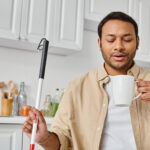 Image of an attractive, visually impaired man holding a cane used for seeing in one hand and a coffee cup in the other. He appears to be looking down as his coffee, implying the cure for blindness could be coming into focus.