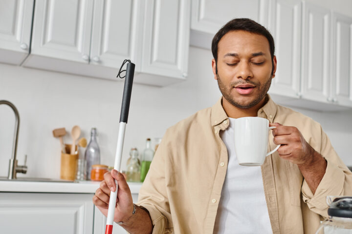 Image of an attractive, visually impaired man holding a cane used for seeing in one hand and a coffee cup in the other. He appears to be looking down as his coffee, implying the cure for blindness could be coming into focus.