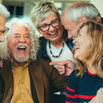 A diverse group of joyful older adults laughing and sharing a moment together, highlighting the importance of social engagement for healthy aging and mental well-being, as emphasized in the blog post about the benefits of staying socially connected.