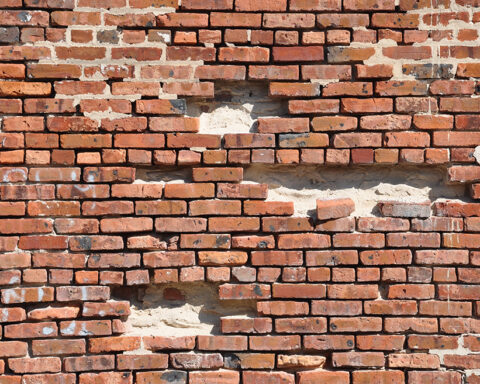 A weathered red brick wall with multiple missing and crumbling bricks, revealing gaps and structural weaknesses. This visually symbolizes genomic instability—how accumulating DNA damage over time weakens cellular function, leading to aging and disease. The deteriorating wall represents the gradual breakdown of the body's genetic integrity, akin to mutations and repair failures that drive the aging process.